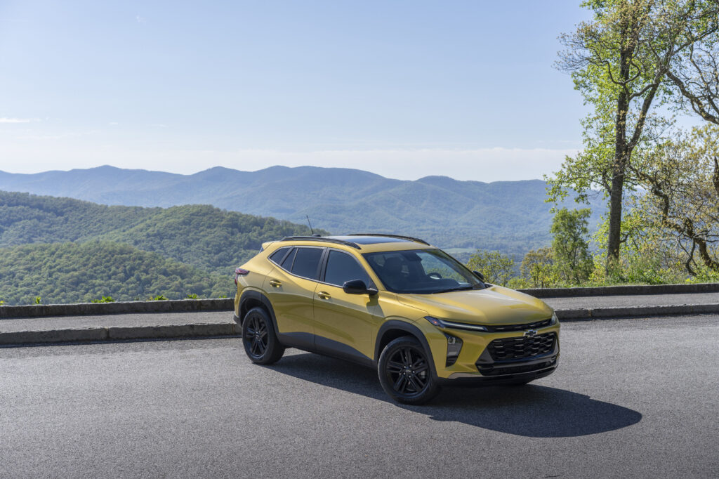 Front 3/4 view of 2024 Chevrolet Trax ACTIV in Nitro Yellow Metallic parked on a road with mountains in the horizon.