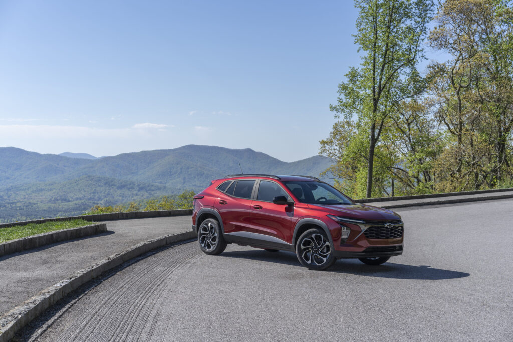 Front 3/4 view of 2024 Chevrolet Trax RS in Crimson Metallic parked on a road with mountains in the horizon.