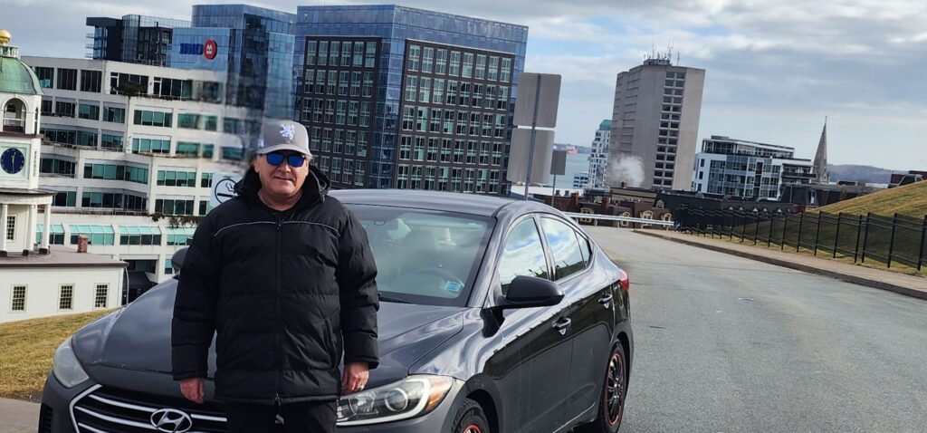 Tim German standing with his Hyundai Elantra at Halifax Citadel National Historic Site overlooking downtown Halifax