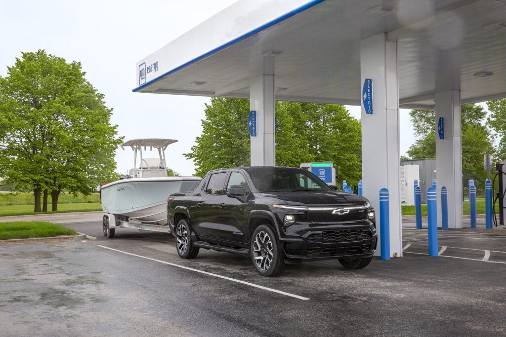 2024 Silverado EV RST towing a boat, while pulling into a GM Energy charging station.